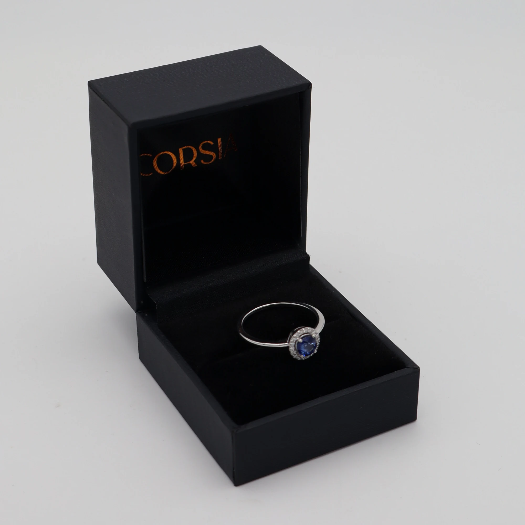 Anillo de compromiso con zafiro redondo y orla de diamantes oro blanco corsia
