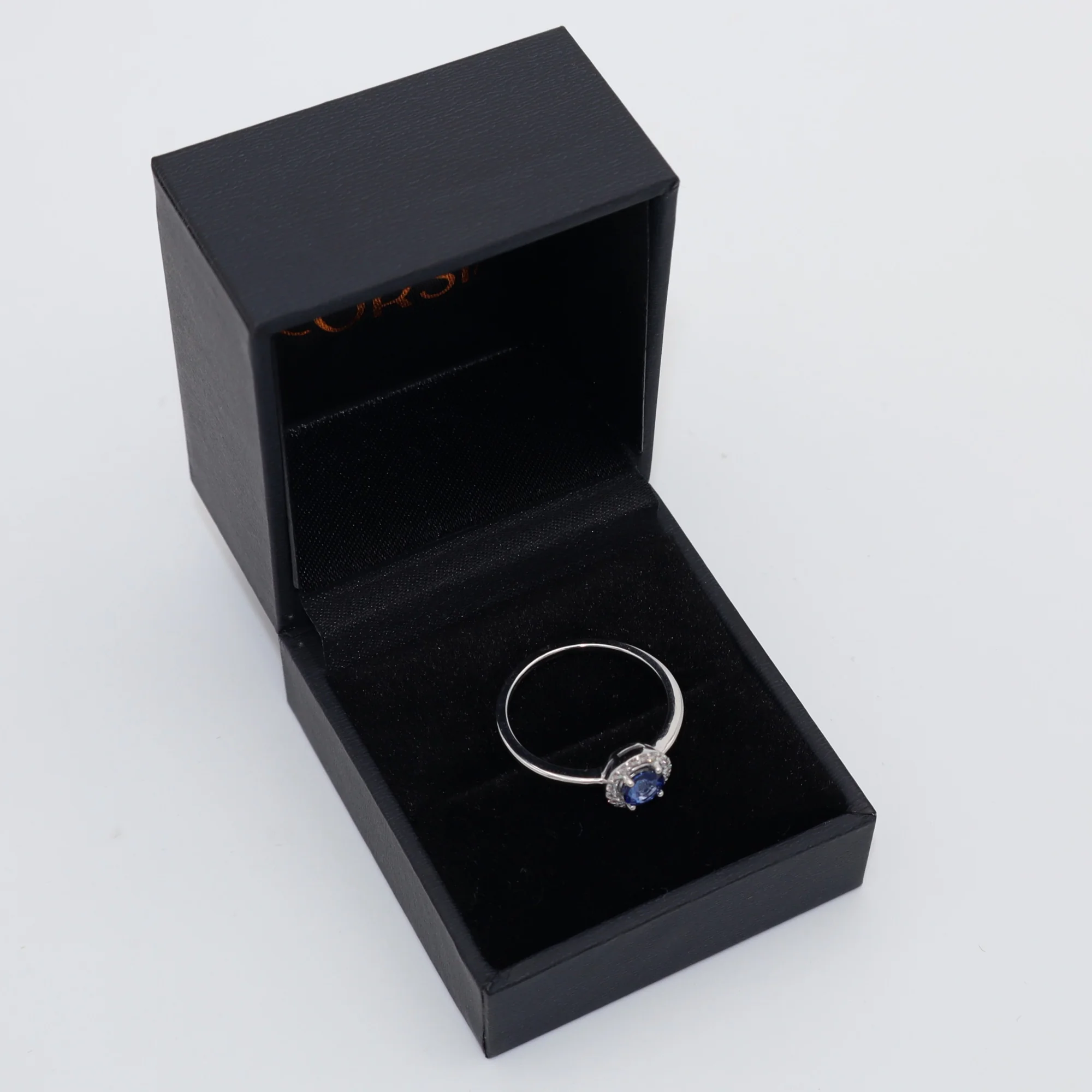 Anillo de compromiso con zafiro redondo y orla de diamantes oro blanco corsia