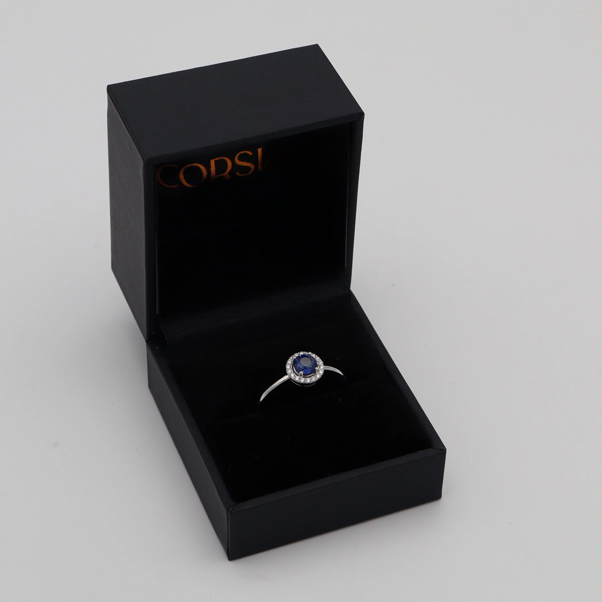 Anillo de compromiso con zafiro redondo y orla de diamantes oro blanco corsia