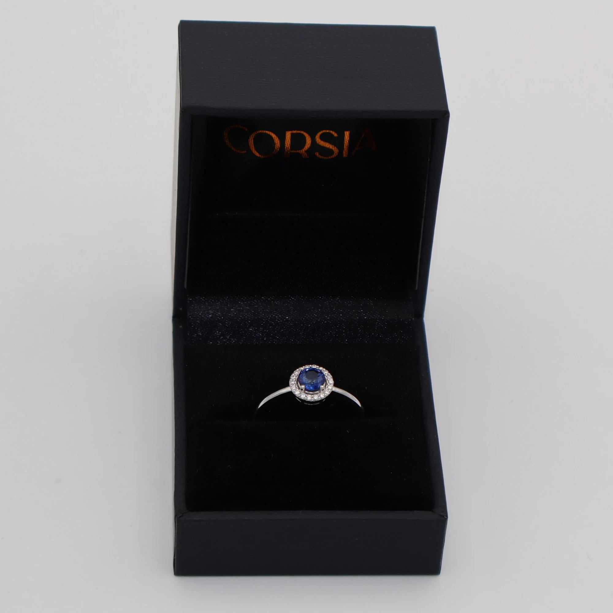 Anillo de compromiso con zafiro redondo y orla de diamantes oro blanco corsia