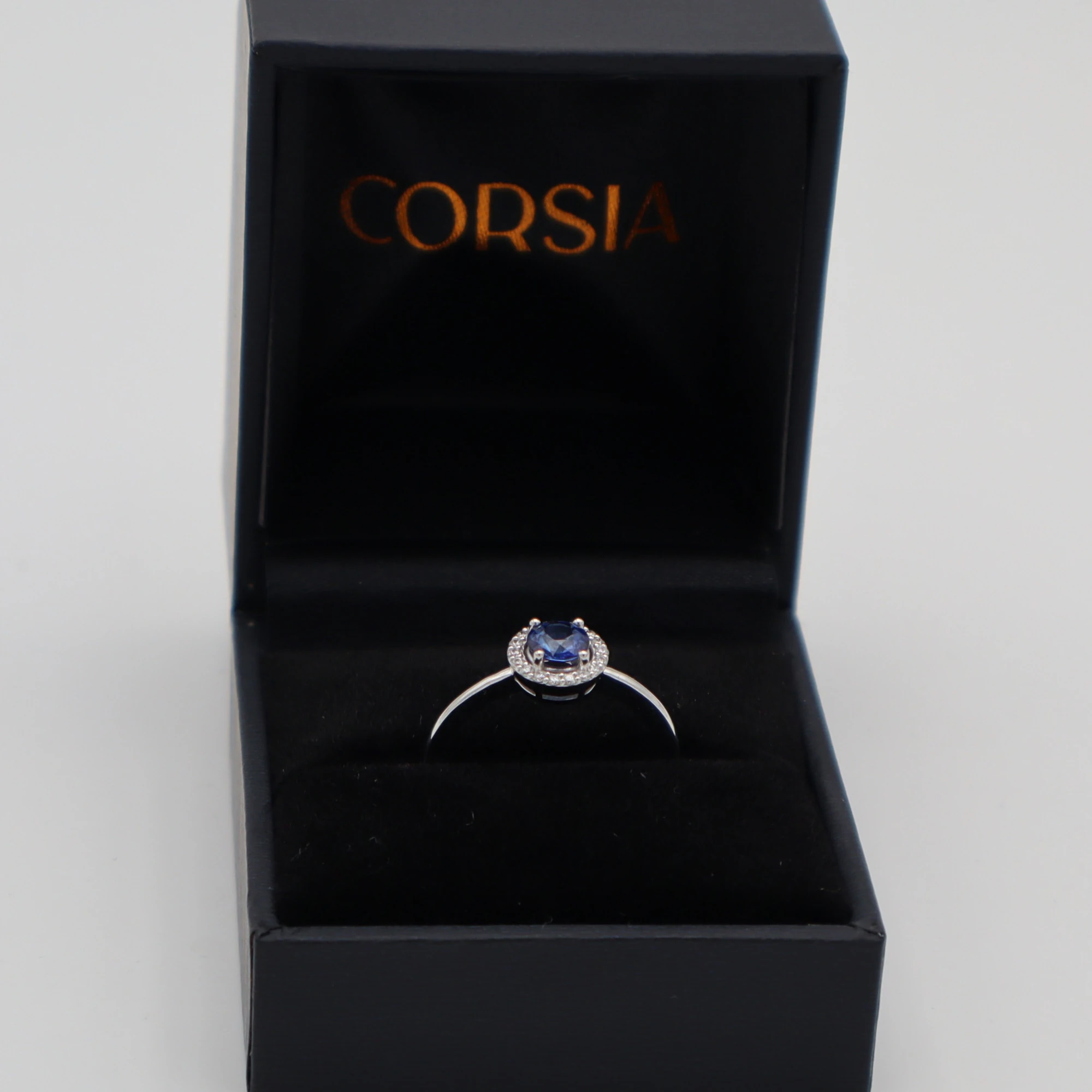 Anillo de compromiso con zafiro redondo y orla de diamantes oro blanco corsia